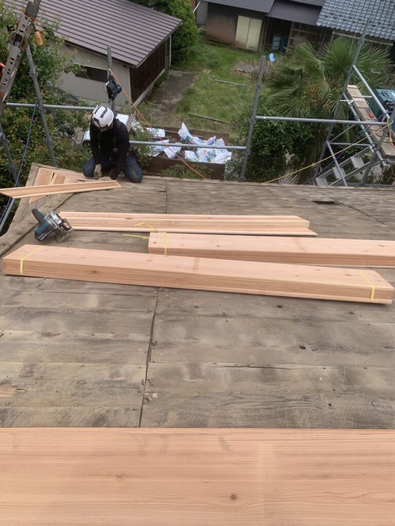 既存の瓦を剥がし、野地板（下地材）が傷んでいるところを補修しました。板が見えています。こちらは県産材の杉板です。増し張りして強度を上げます。